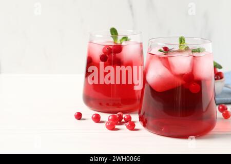 Tasty cranberry juice with ice cubes in glasses and fresh berries on white wooden table, closeup. Space for text Stock Photo