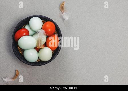 Blue and red colored eggs in a basket and bird feathers top view, Easter composition Stock Photo