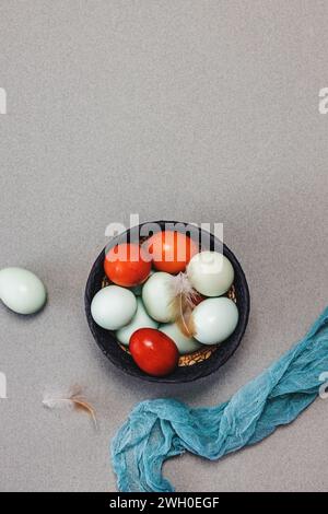 Naturally blue and red colored eggs in a basket and bird feathers top view, Easter composition Stock Photo