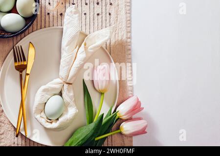 Easter table setting, napkin folded in shape of a rabbit , blue egg and pink tulips. Spring still life, top view Stock Photo