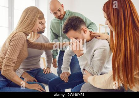 People in group therapy comforting, supporting and trying to help sad depressed man Stock Photo