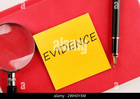 EVIDENCE the inscription on the sticker lying on a red notebook next to a magnifying glass and a fountain pen Stock Photo