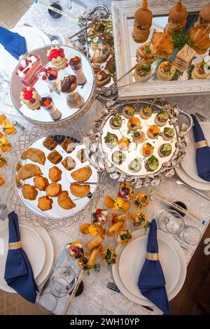 A beautifully decorated table is laden with a variety of delicious appetizers and desserts and elegantly set with white tablecloths and napkins, creat Stock Photo