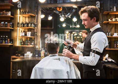 Handsome barber spraying water over head. Professional hairdresser preparing hair for cutting. Young client getting stylish hairstyle. Stock Photo