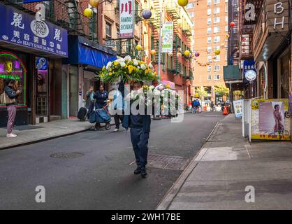 A man carries two large flower arrangements down Chinatown street NYC Stock Photo