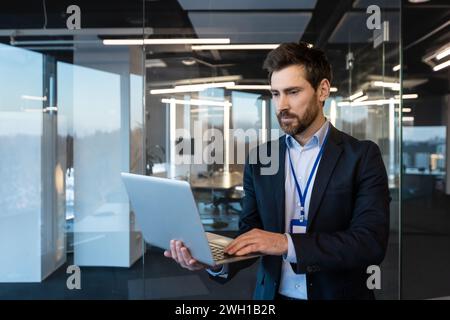 Focused mature businessman working in a modern office, analyzing data on his laptop, representing leadership and determination. Stock Photo