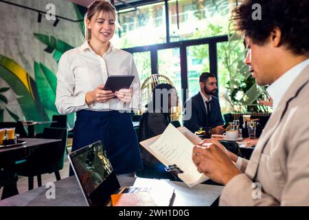 Smiling waitress taking orders from African American businessman in restaurant. Stock Photo