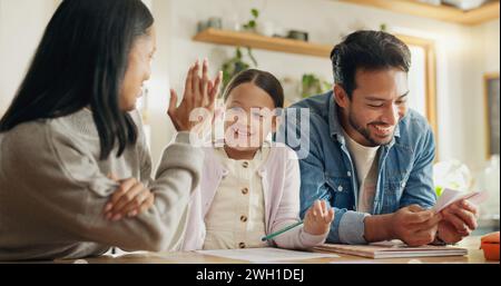 High five, girl with parents and support with learning in house with card, game or mom and dad helping with homework together in home. Child, family Stock Photo