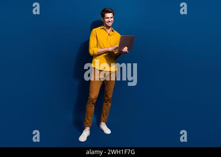 Full length photo of nice young male hold netbook working manager dressed stylish yellow garment isolated on dark blue color background Stock Photo