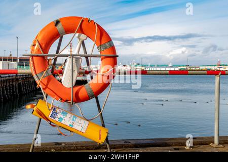 Orange lifebuoy along with rope while drowning rescuing kit and medical assistance placed together on metal stand near pier fence in port against clou Stock Photo
