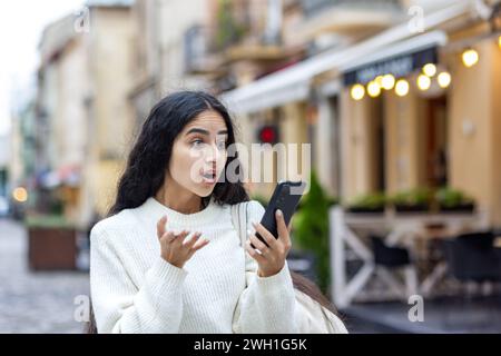A young Indian woman shows surprise while using her phone on a city walk a tourist enjoying urban exploration and sightseeing. Stock Photo