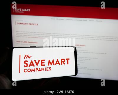 Person holding mobile phone with logo of American supermarket company The Save Mart Companies in front of web page. Focus on phone display. Stock Photo