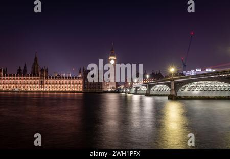 London. UK- 02.04.2024. A long exposure night time view of the Palace of Westminster, Big Ben and Westminster Bridge casting light reflections on the Stock Photo
