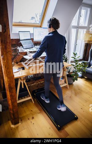 Eine Frau laeuft waehrend der Arbeit zu Hause im Home Office an ihrem Schreibtisch auf einem Walking Pad. Berlin, 07.02.2024. Berlin Deutschland *** A Stock Photo