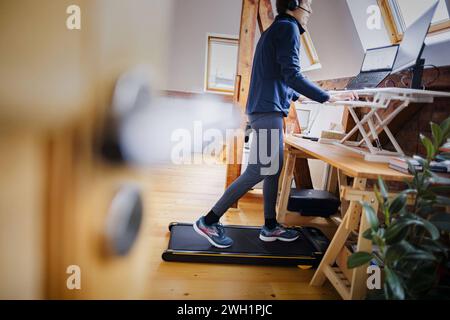 Eine Frau laeuft waehrend der Arbeit zu Hause im Home Office an ihrem Schreibtisch auf einem Walking Pad. Berlin, 07.02.2024. Berlin Deutschland *** A Stock Photo