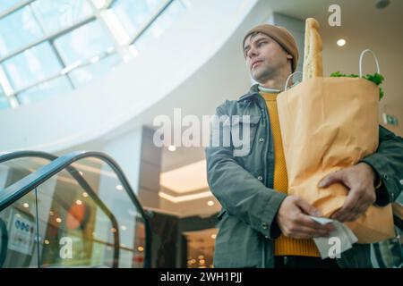 Man holds paper bag filled with various food items in his hand in mall Stock Photo