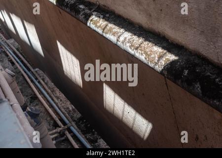 Sunlight piercing through an obstruction creates a distinct pattern of shadows on a textured wall, indicating a sunny day. Stock Photo