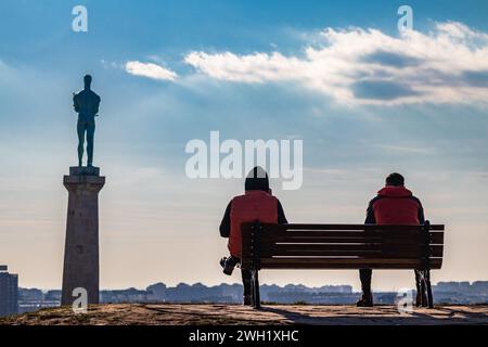 Two friends outdoors on nice sunny day, sitting on the bench at Kalemegdan fortress in Belgrade, with beautiful view on statue of victory (Pobednik) Stock Photo