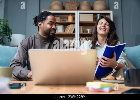 Young smart couple business owners and partners architectural exterior interior designers working from home on laptop computer with blueprint and colo Stock Photo