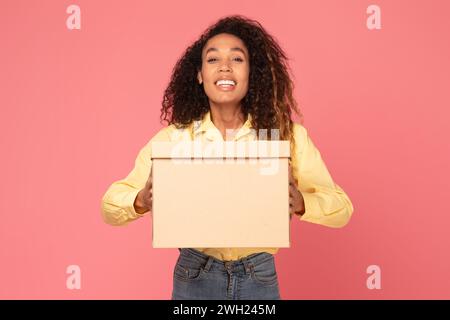 Young black woman smiles holding parcel on pink backdrop Stock Photo