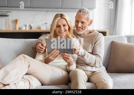 Excited smiling senior spouses using digital tablet computer at home Stock Photo