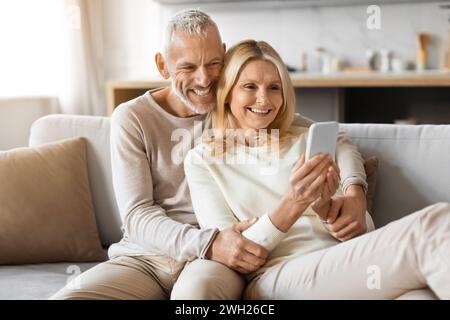 Happily married senior couple scrolling on social media, using phone Stock Photo