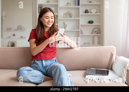 Happy young asian woman using smartphone and laptop at home Stock Photo