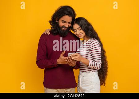 Loving young indian couple using cell phone on yellow Stock Photo