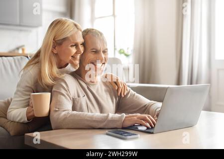 Excited smiling senior spouses using laptop computer at home Stock Photo