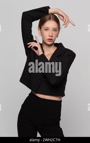 In a black fashionable suit, a young girl poses against a gray background. Stock Photo