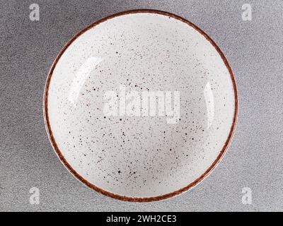 White empty deep clay plate with a spoon on a gray background. Stock Photo