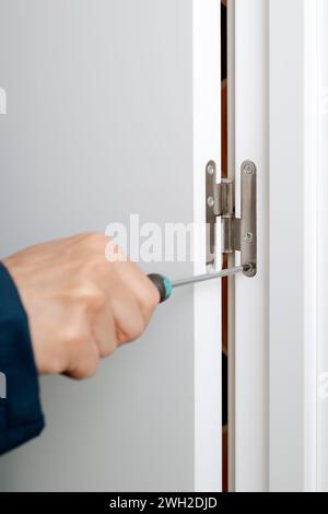 closeup of a caucasian man, wearing blue overalls, screwing or unscrewing the hinge of a door using a screwdriver Stock Photo