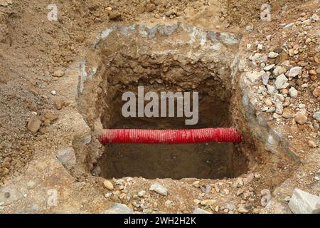 Street maintenance excavation with exposed red PVC protective pipe for underground cables and wires in Morocco. Stock Photo