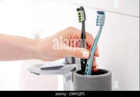 Girl'S Hand Places Two Toothbrushes In Cup For Hygiene In Bright Bathroom Stock Photo
