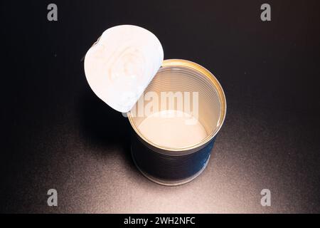 View into an anready opened and empty food can with white coating inside. Can lid is bend back. Dark background. Stock Photo