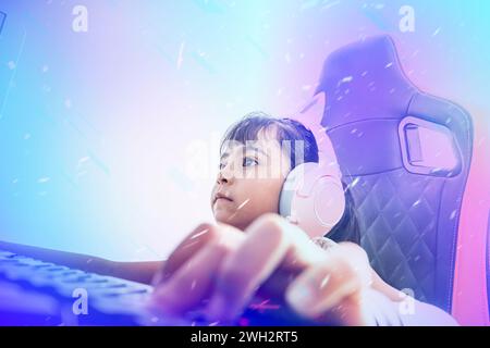 Composition with bright colors of a cute little girl playing on the computer in the bedroom. She is a girl streamer wearing pink headphones and sittin Stock Photo