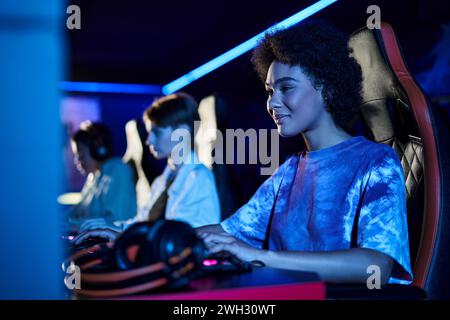 pleased african american woman looking at monitor in blue lit room, playing computer game Stock Photo