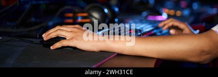 cropped shot of woman using computer mouse near illuminated keyboard while playing game, banner Stock Photo