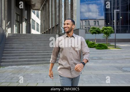 Energetic muslim male agent walking down street with satisfied facial expression. Optimistic agent leaving office building after profitable productive day and feeling excited about weekend ahead. Stock Photo