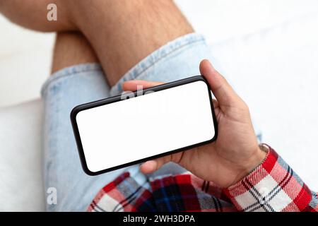 Directly above photo of smart phone with empty screen in hand of man. Male person sit on sofa and use mobile phone high angle view. Stock Photo