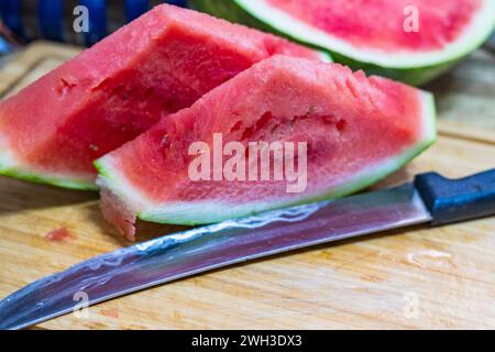 two slices of watermelon on a cutting board next to a knife. Stock Photo