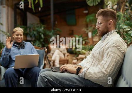 Side view portrait of bearded businessman using laptop doing research online in green coworking space Stock Photo