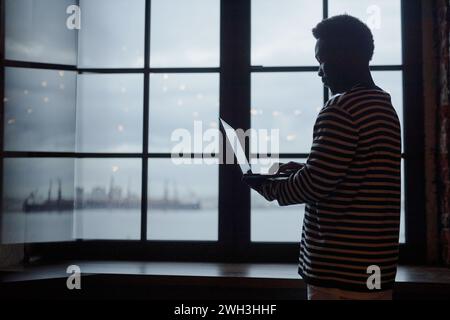 Backlit outline of African American man using laptop standing by graphic window copy space Stock Photo