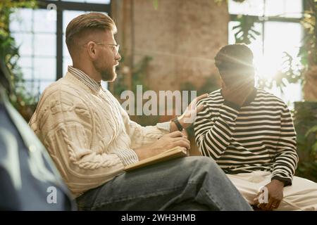 Side view portrait of bearded male psychologist supporting client during therapy session with lens flare Stock Photo