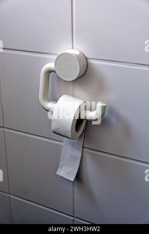 Toilet paper holder with mini roll of paper on a tiled wall Stock Photo