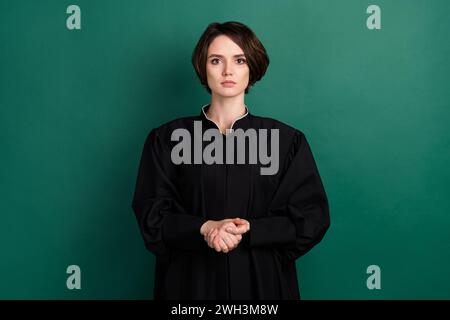 Photo of beautiful serious confident judge woman attorney wearing long black robe isolated on green color background Stock Photo