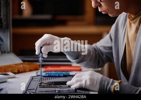 Close-up of repairman fixing broken smartphone with screwdriver sitting at table in workshop Stock Photo