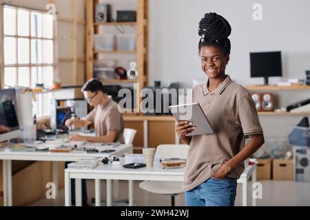 Black entrepreneur posing in workshop holding digital tablet, male repairman working on background Stock Photo