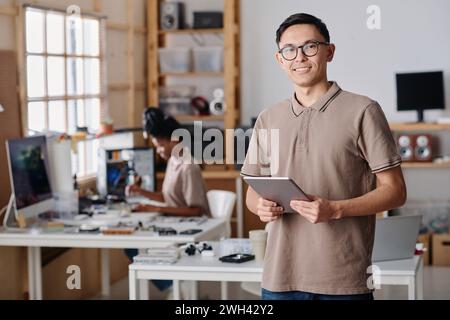 Male workshop owner confidently posing at workplace, black female technician working on background Stock Photo