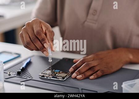 Hands of unrecognizable black specialist tightening cogs in disassembled phone with little screwdriver Stock Photo